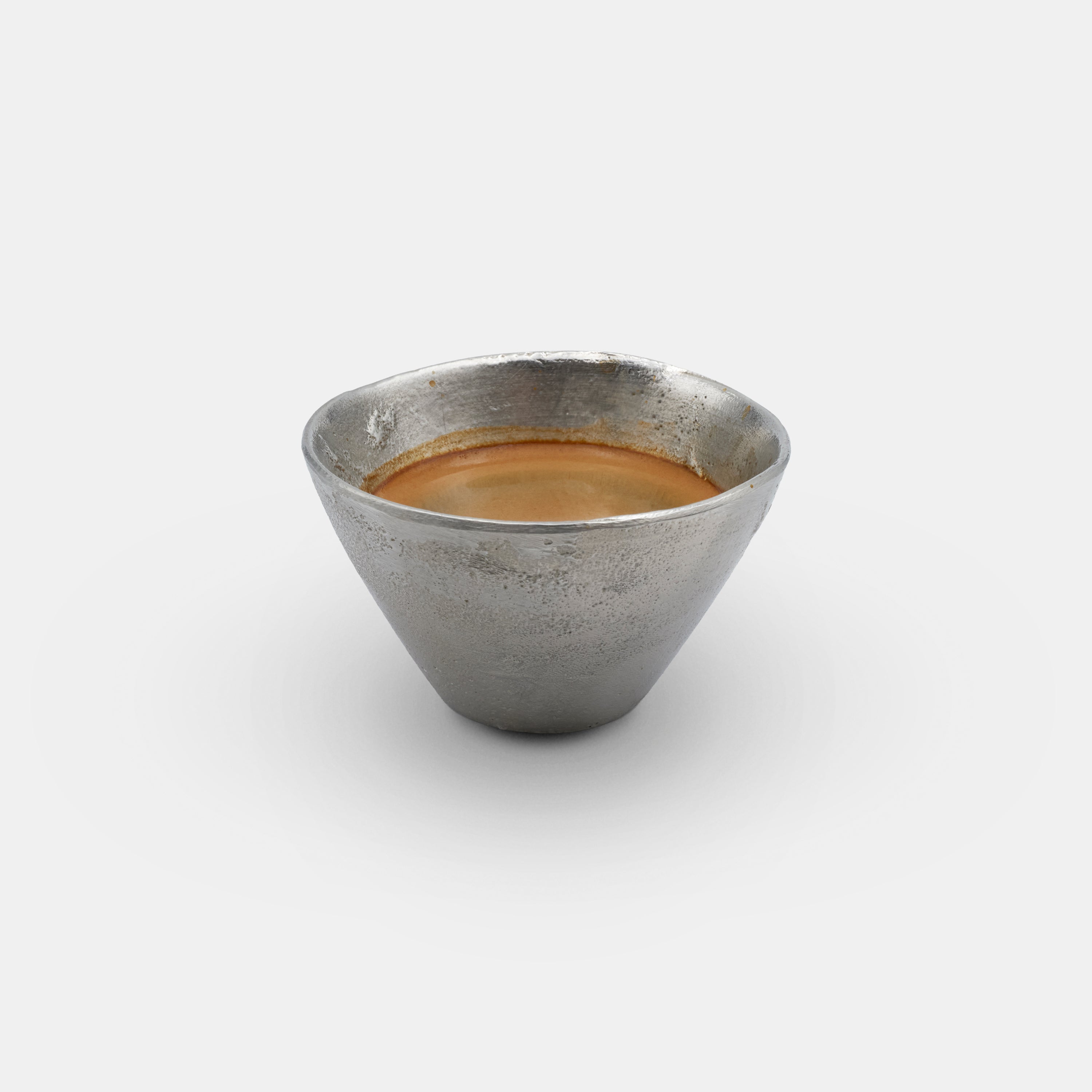 OFFFHAND HOLD Cup made from pure silver, filled with coffee and photographed in a studio setting.