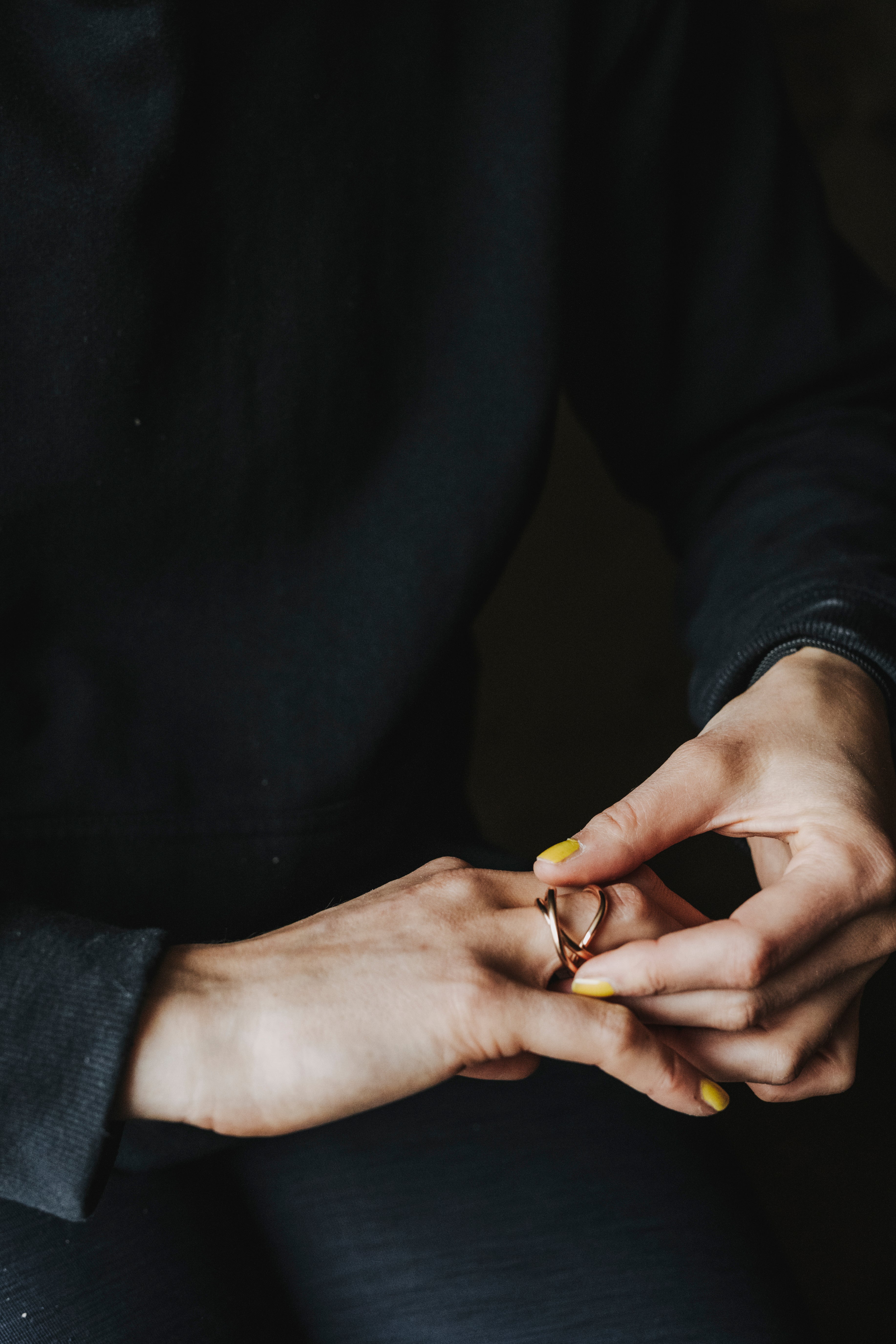 Close-up of a person from the front, wearing black clothing against a black background. One hand wears a ring from the Saturnian collection.
